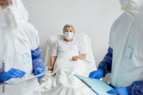 Two unrecognizable doctors standing in hospital ward with elderly female patient on bed discussing something