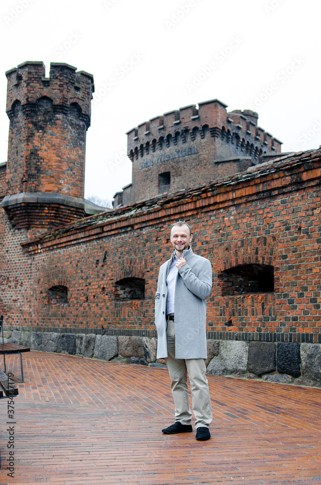 Handsome businessman freelancer in grey coat and biege trousers smiles on historical background