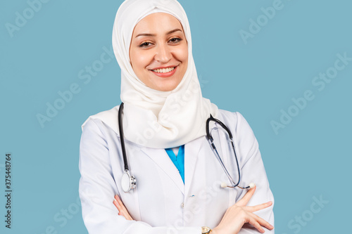 Portrait of a friendly, Muslim doctor or nurse woman in hijab with a stethoscope in a white coat. on a blue background.