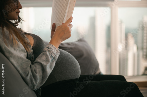 pregnancy concept - pregnant woman on sofa and reading book (ID: 375448772)
