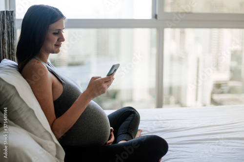 Pregnancy young woman texting on mobile phone on bed (ID: 375449144)