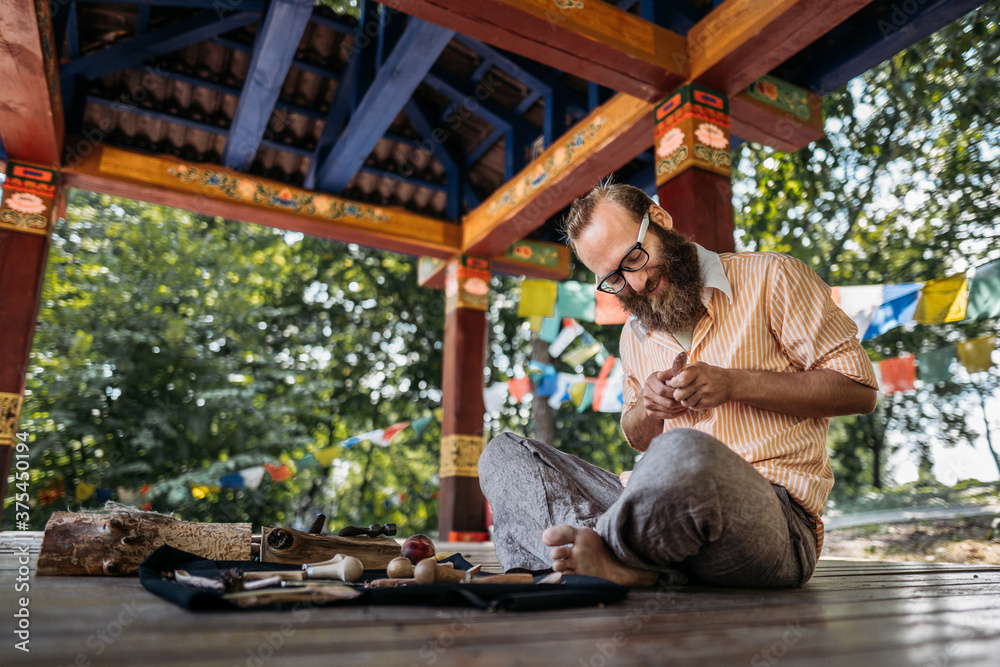 a man with glasses holding a tool for a tree in his hands and making a product in a park sitting on the floor in a stylized eastern zone