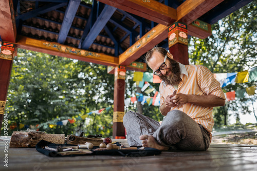 a man with glasses holding a tool for a tree in his hands and making a product in a park sitting on the floor in a stylized eastern zone