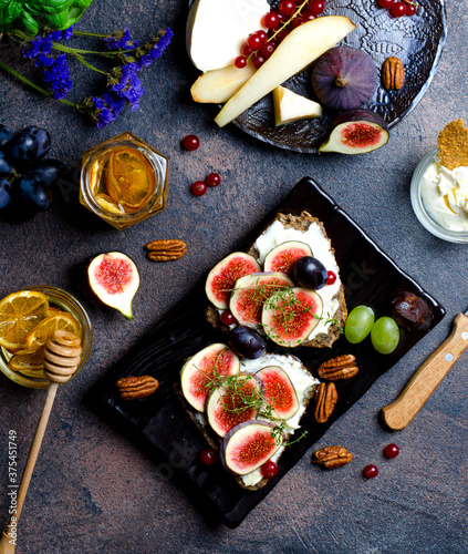 Morning snack with fig sandwiches, fruit, berries, honey and nuts, vertical closeup