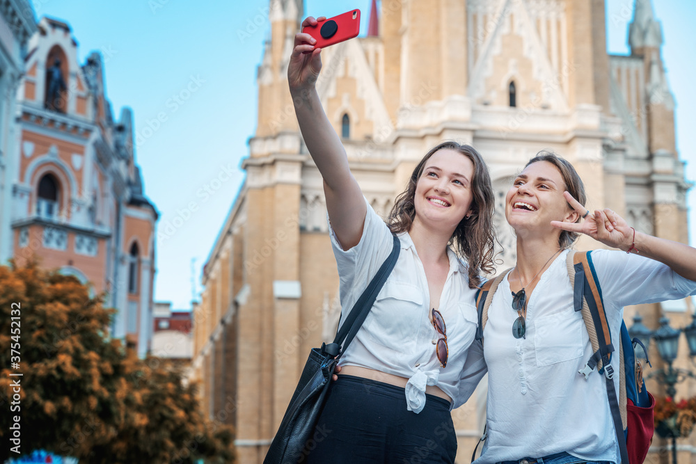 Two young happy pretty female students taking selfie on a mobile phone against the background of a european city