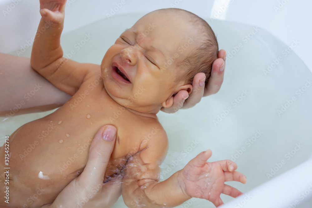 A small newborn girl is bathing in a bath for the first time A small newborn girl is bathing in a bath for the first time