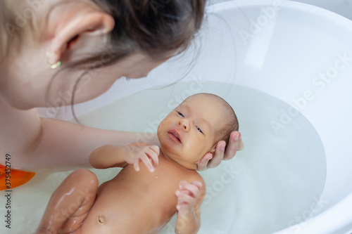 Mother bathes a newborn for the first time in a bath holding his head