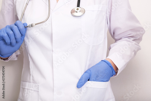 A doctor in white uniform and blue rubber gloves holding stethoscope, professional expertise and testing concept