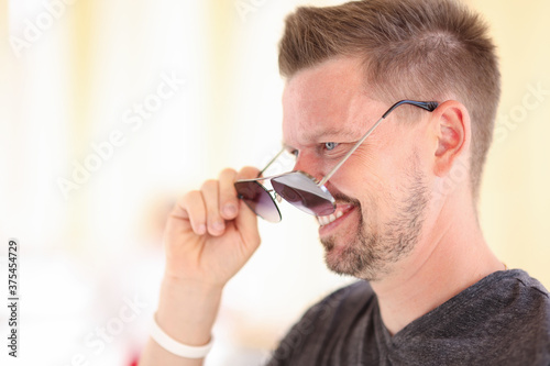 Man stands in profile and measures his sunglasses. Fashionable glasses for men concept