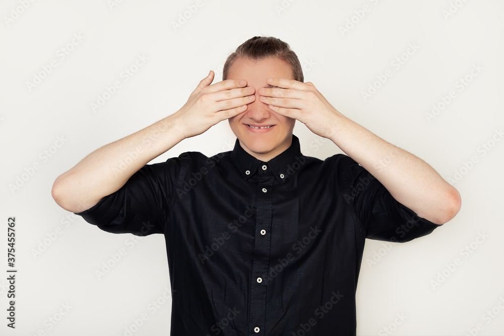 Handsome young guy student in a black shirt, smiling, closed his eyes with his hands so as not to see, cheerful and funny. Blind concept. Handsome young guy student in a black shirt, smiling, closed his eyes with his hands so as not to see, cheerful and funny. Blind concept.