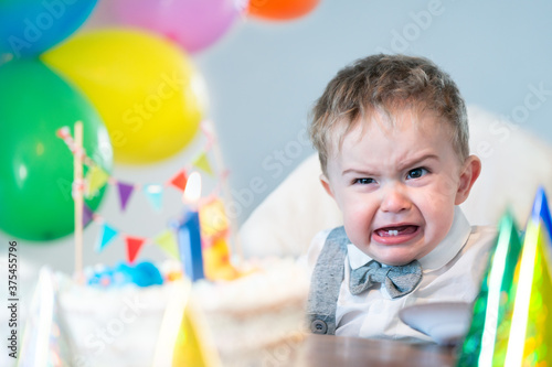 Photo Crying boy with birthday cake and balloons