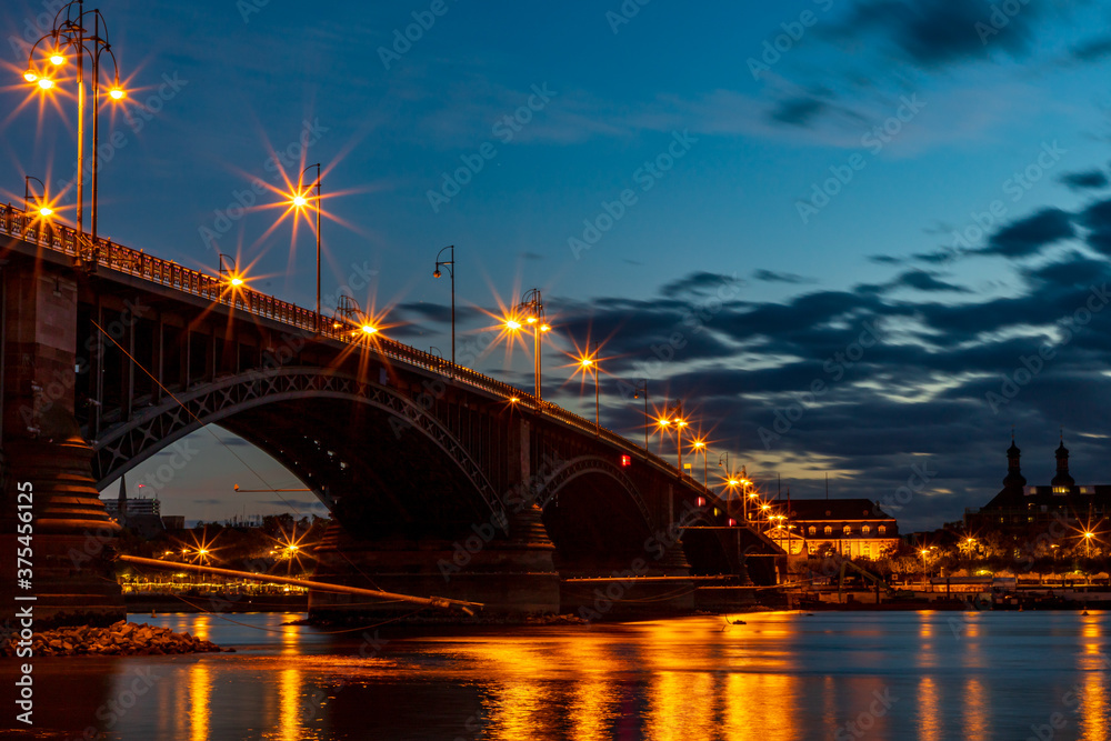 Obraz premium The illuminated Theodor Heuss Bridge that crosses the Rhine between Mainz and Wiesbaden at night. In the background the silhouette of Mainz