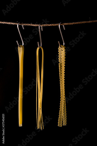 Close-Up Of Raw Pasta Hanging On String Against Black Background