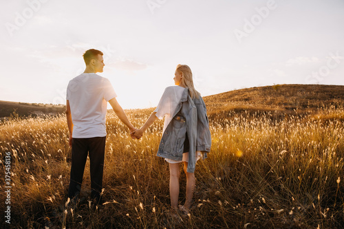 Young romantic couple standing in an open field with dry grass, holding hands.