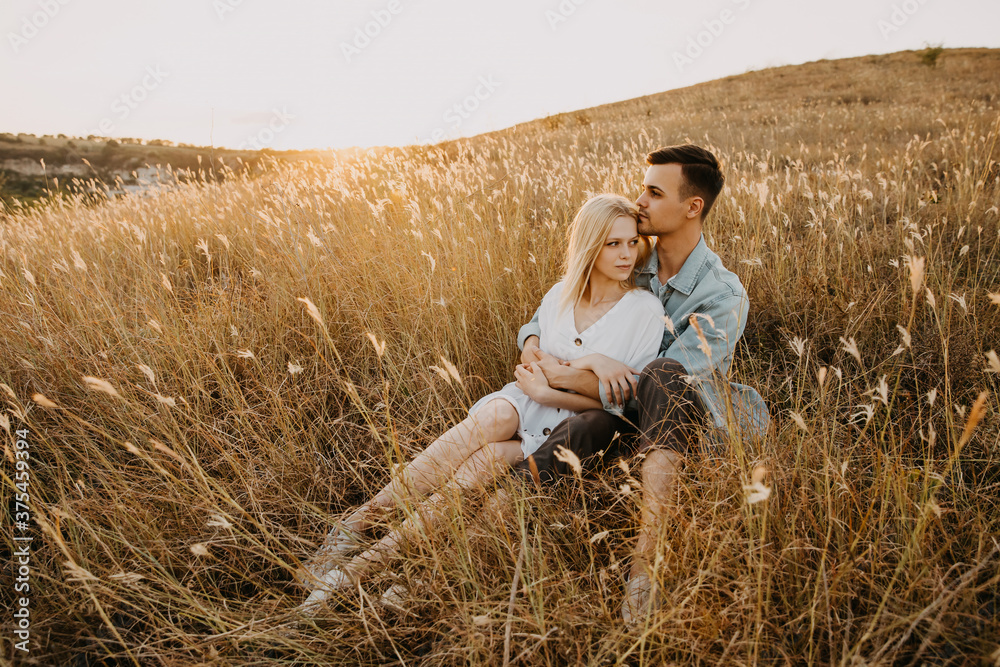 Young couple of man and woman sitting in a golden field, hugging. Young couple of man and woman sitting in a golden field, hugging.