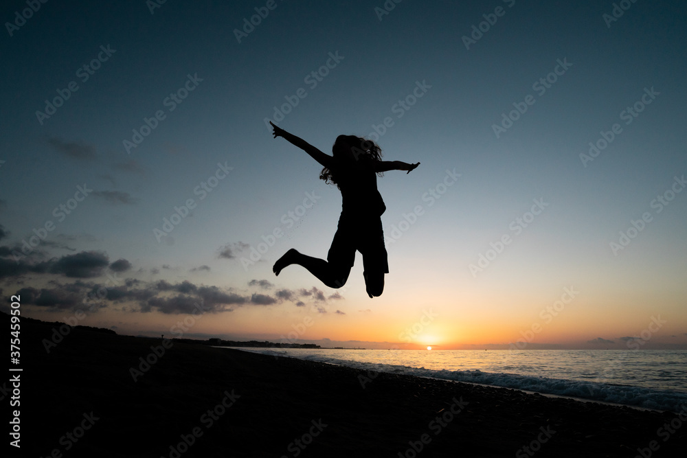 A woman jumps for joy on the beach at dawn. She has achieved her goal