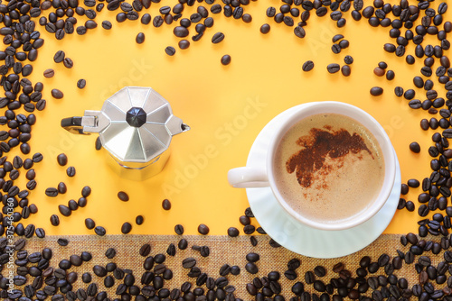 Large cup with coffee with milk and foam, metal coffee teapot, coffee beans on a yellow background photo