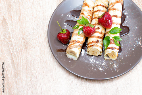 Pancakes with banana and strawberries on a plate. Banana wrapped in a pancake and with strawberries on top. Breakfast with Pancakes with berries and banana and chocolate..