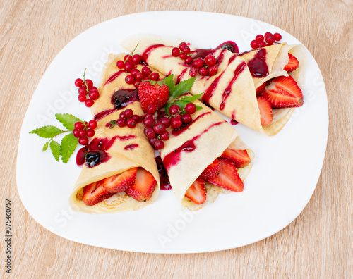 Pancakes with cranberries and strawberries on a plate. Pancakes with berries, strawberries and chocolate syrup. Breakfast with pancakes with strawberries and berries on a plate..