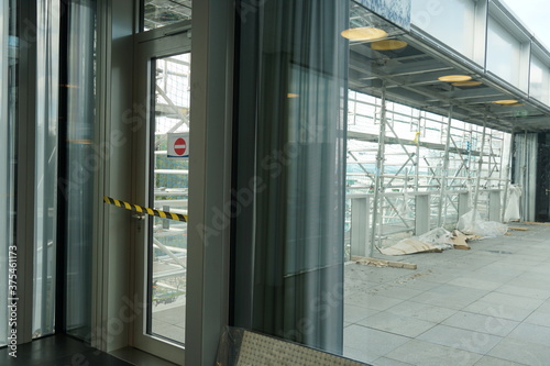 Closed door and blocked with barrier tape and no entry sign to the terrace that is being reconstructed and covered with scaffolding and construction material.