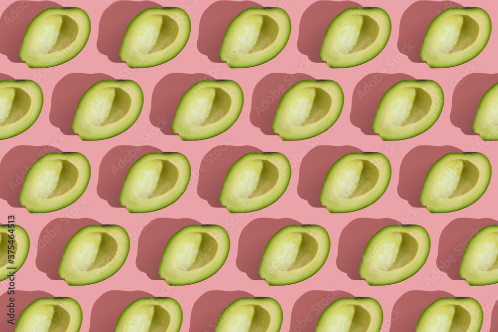 Trending style pattern of half seedless green avocado on pink background with hard light. Creative food texture.