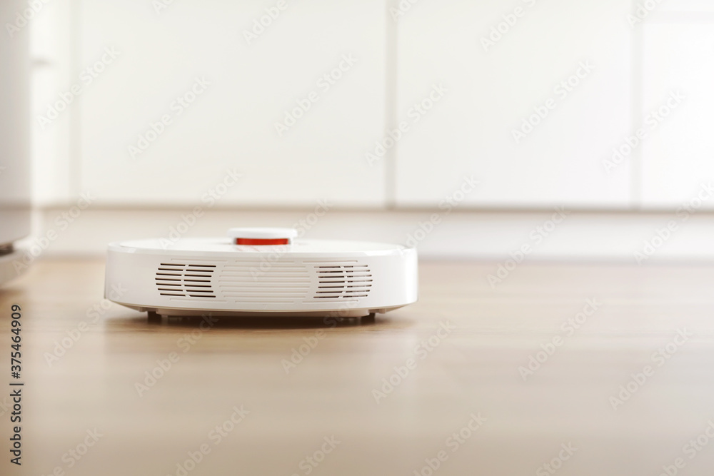 White robotic vacuum cleaner on laminate floor cleaning dust in living room interior. Smart electronic housekeeping technology. smart home White robotic vacuum cleaner on laminate floor cleaning dust in living room interior. Smart electronic housekeeping technology. smart home