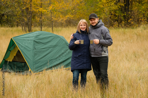 Family is standing near the tent. Man and woman went on a trip to the autumn forest. Outdoor recreation.