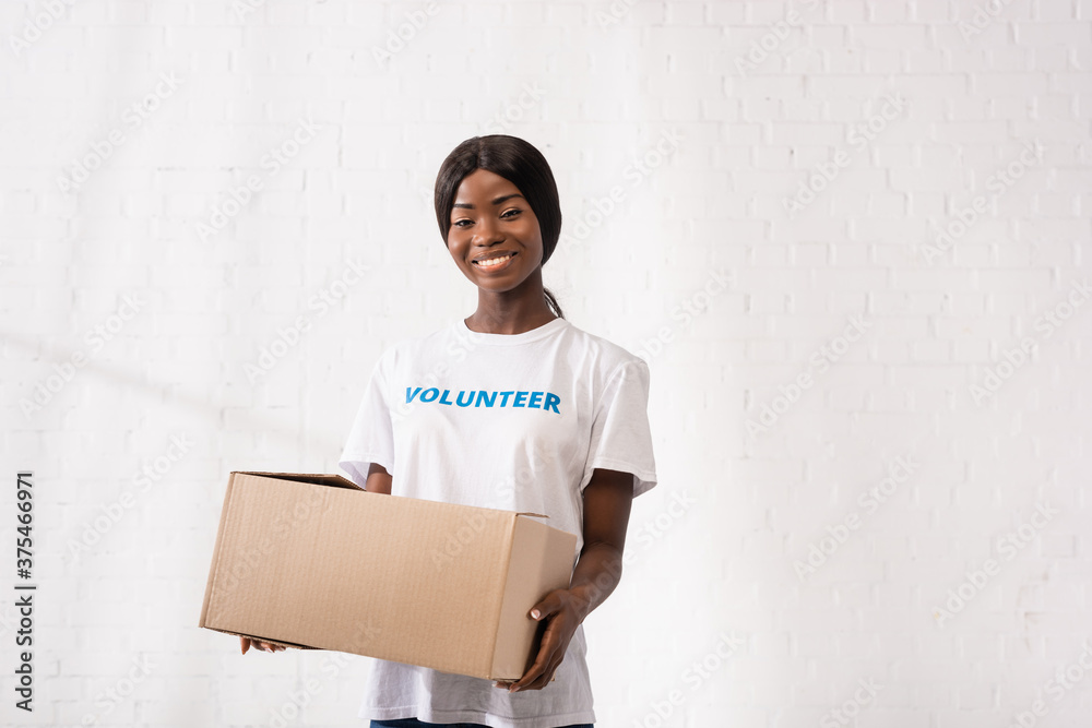 Young african american volunteer with carton box looking at camera in charity center Young african american volunteer with carton box looking at camera in charity center
