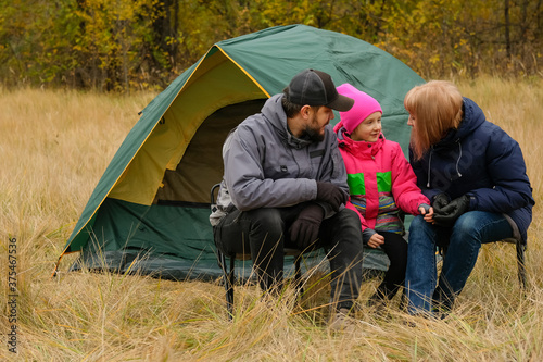 Family is sitting at the tent. Father, mother and daughter went on a trip to the autumn forest. Outdoor recreation for parents and child. © alexeytsurkan