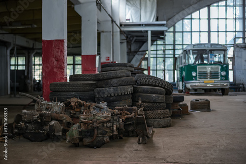 A pile of old car parts and tires in a large garage building with a green retro bus on a bokeh background