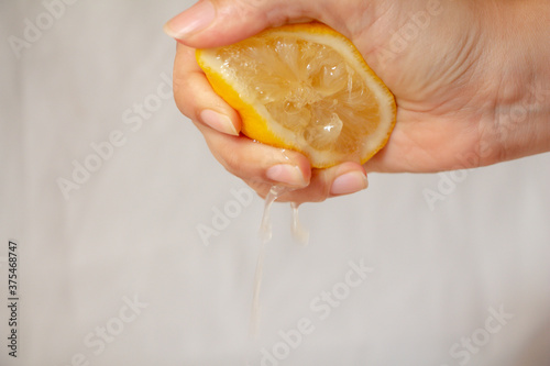Close up female hand squeezing half of lemon on white background.