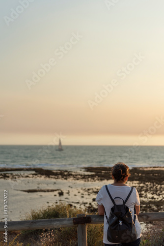 : Mujer con mochila mirando un velero en el mar