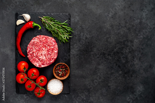 Raw hamburger patties with rosemary and spices on a stone background with copy space for your text