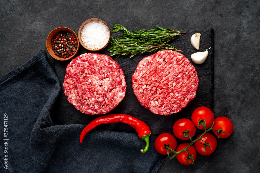 Raw beef burger cutlets with rosemary and spices on a slate board on a concrete background Raw beef burger cutlets with rosemary and spices on a slate board on a concrete background