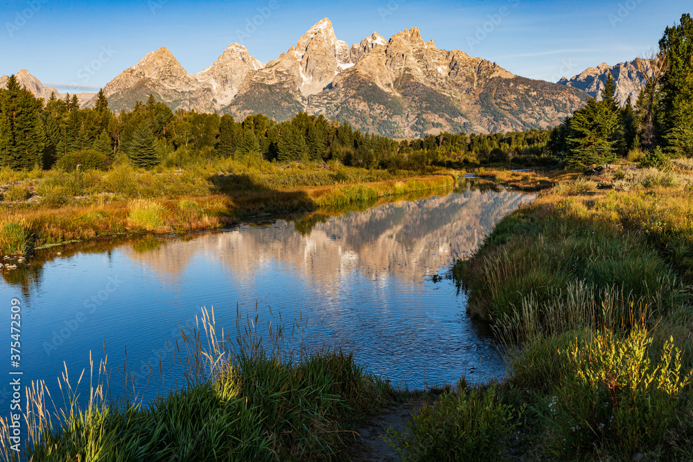 Teton mountains reflect in the water of the Snake river in morning light at Schwabacher Landing in Grand Teton National Park during Fall