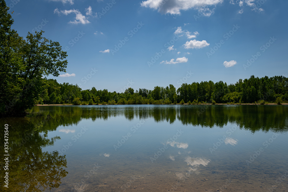 Obraz premium Puffy white clouds floating over and reflecting in a beautiful inland lake on a bright autumn afternoon.