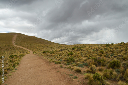Hiking. The dirt path along the hill and yellow grassland under a cloudy sky. 