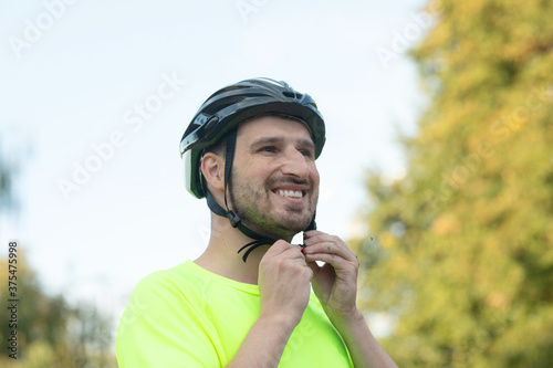 Handsome young man putting on bicycle helmet in park. © lashkhidzetim