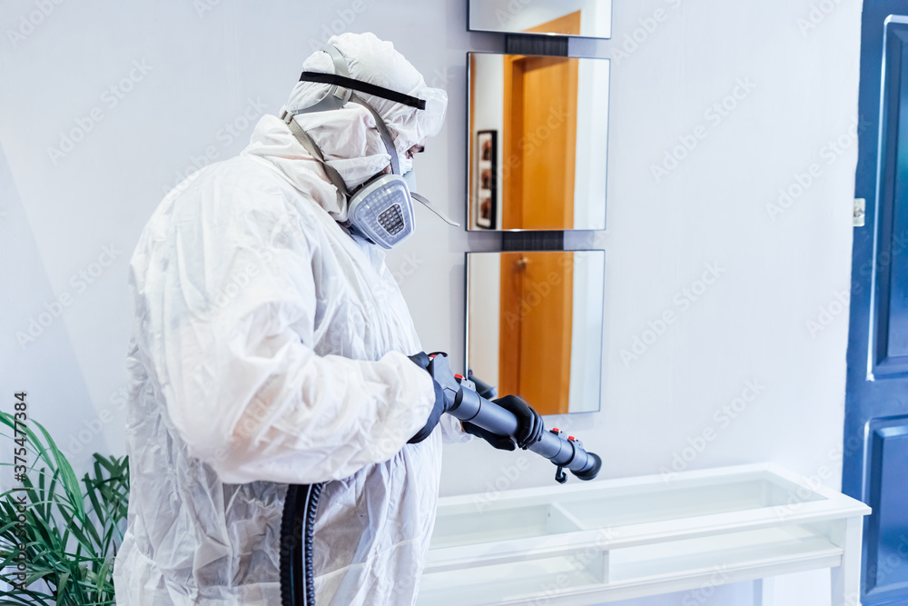 Man wearing PPE inside a house disinfecting a glass table from COVID-19. Pandemic healthcare concept