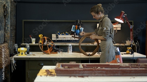 Restoration of wooden chair in a workshop. A working female carpenter peels off paint from a wooden product with a spatula, restorer in a workshop, gimbal shot