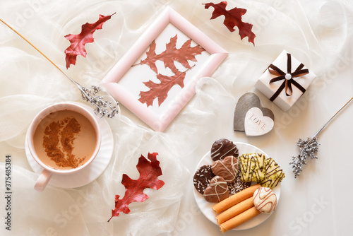 Coffee cap, chocolate chip cookies on a plate,wooden hearts,gift box,red autumn leaves on bage table