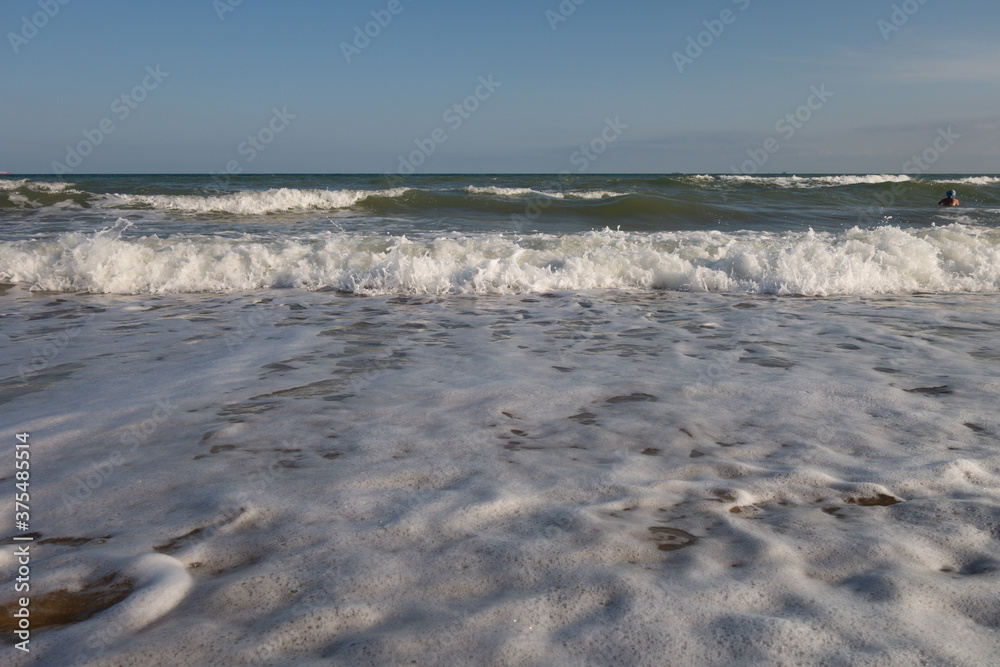 Sandy seashore, foamy oncoming waves and a beautiful sky on a summer sunny day.