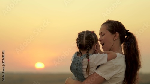 Mom plays with her daughter and shows the child the sunset. Happy family, mom and daughter in the field look at the sun. The concept of happy family and healthy children. baby loves mommy