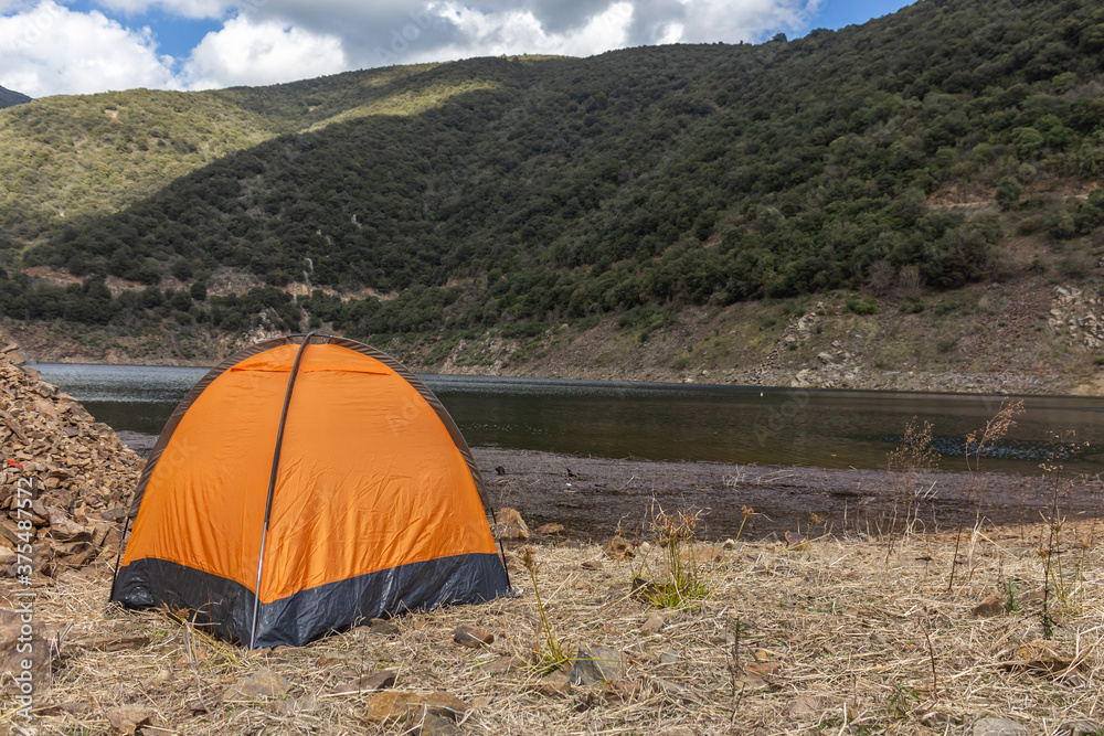 Orange camping tent in front of a lake
