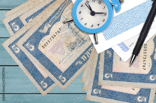 5 Ukrainian hryvnias bills and alarm clock with pen and envelopes. Tax season concept, payment deadline for credit or loan. Financial operations using postal service photo