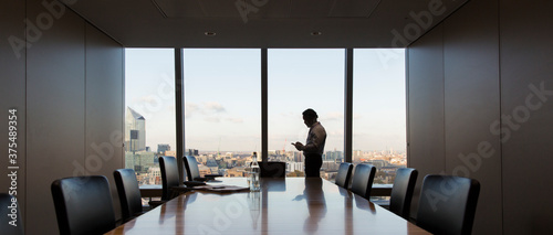 Businessman using smart phone at highrise conference room window photo