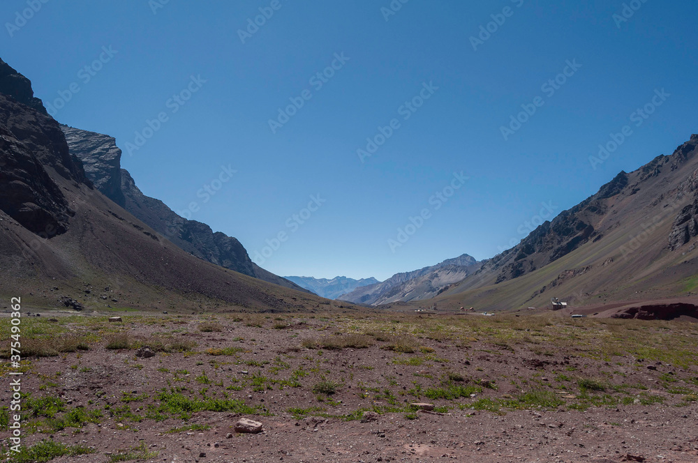 Coordillera de los Andres, paso Argentina Chile, montañas en cielo azul despejado cubiertas por cesped natural.