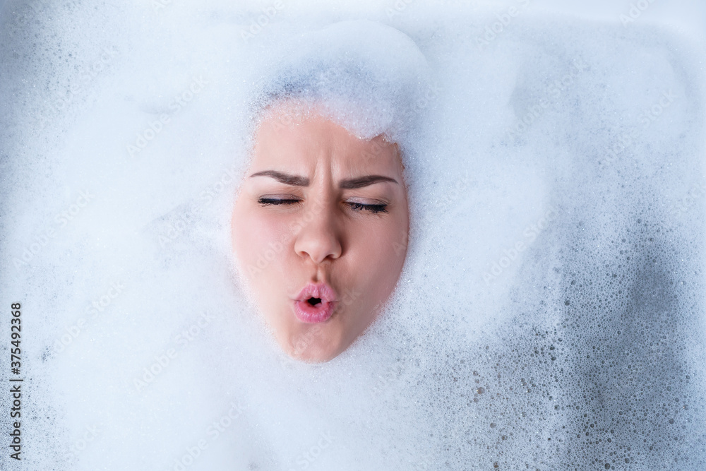Closeup portrait of a girl in a bathtub and white foam around her face. Different emotions, grimaces, woman smile Closeup portrait of a girl in a bathtub and white foam around her face. Different emotions, grimaces, woman smile