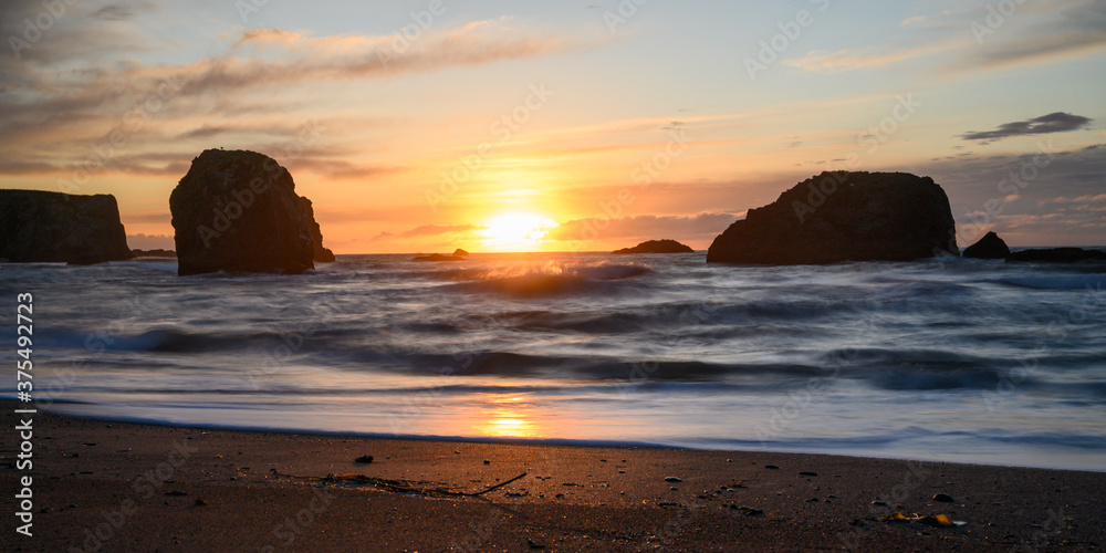 Sun setting between silhouetted rocks in the ocean. Lots of space for text. 