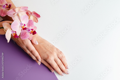 Young woman s hands close-up. Stylish trendy manicure on white and purple background. Tropical orchid flowers. Place for text. Advertising of manicure and beauty salon. Relaxation spa service